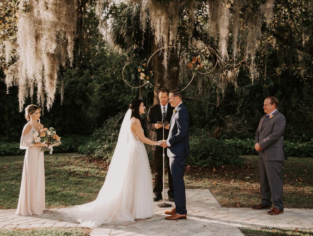 bride and groom holding hands during outdoor wedding ceremony under large oak tree with spanish moss